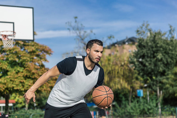 attraktiver und starker Stadtspieler spielt an einem schönen, sonnigen Sommertag im Freien Basketball - Foto, Bild