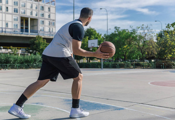 Urban speler speelt basketbal alleen op een stedelijk veld van een grote stad - Foto, afbeelding