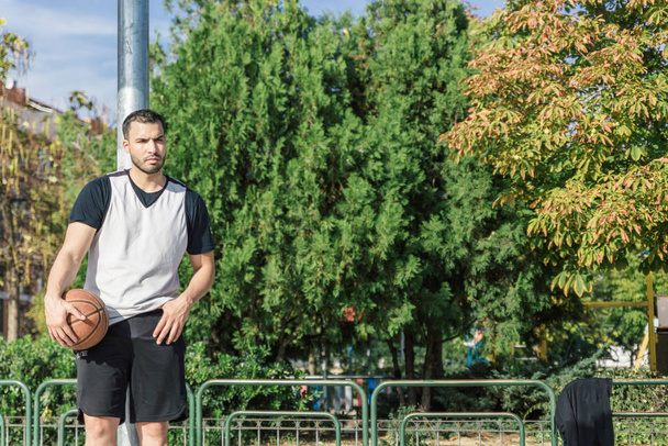 Aantrekkelijke urban basketbalspeler leunend op een metalen kolom op een veld - Foto, afbeelding