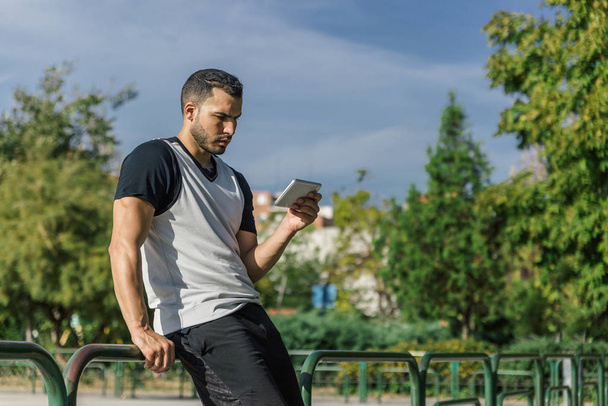 Aantrekkelijke sterke sportman leest op een tablet op een stadsplein - Foto, afbeelding