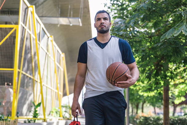 Detailní záběr pohledného a atraktivního mužského atleta latinského původu, nesoucího svůj basketbal při chůzi po ulici - Fotografie, Obrázek