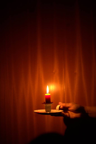 Kaarslicht schijnt in het donker tegen een houten achtergrond. Stroomuitval, black-out concept. - Foto, afbeelding