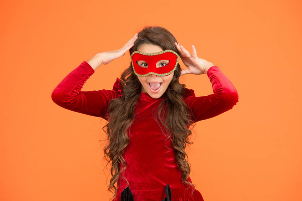 Visit public event anonymously. Winter new year party. Winter carnival. Incognito mode. Kid wear eye mask. Girl wear mask orange background. Winter event and entertainment. Child development - Fotografie, Obrázek