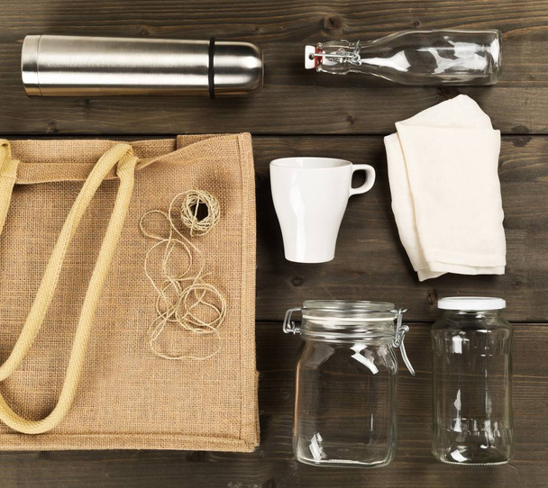 Zero waste or waste free shopping utensils with burlap bag, glass bottles and cotton bag on brown wooden table background  - Valokuva, kuva
