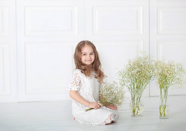 little girl with a bouquet of gypsophila. Portrait of a charming girl with blond hair in a white dress holding flowers. March 8, International Women's Day, Mother's Day. Cute baby with a bouquet. - Valokuva, kuva