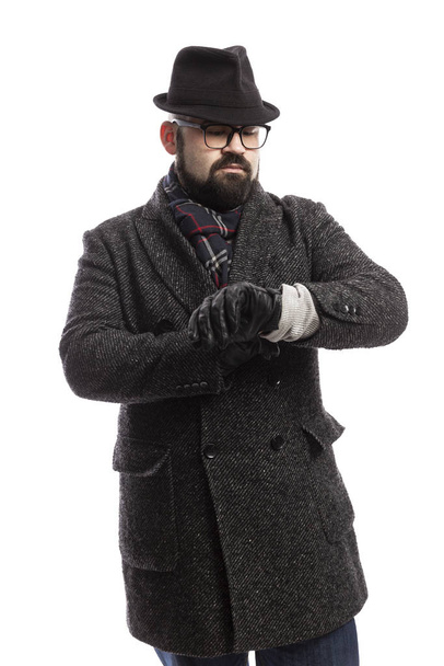 Elegant man with a beard in a coat and hat looks at his watch. White background.  - Фото, зображення