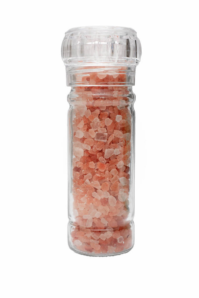 白い背景に隔離されたガラス製のグラインダーボトルにピンクのヒマラヤ結晶塩のクローズアップ - 写真・画像