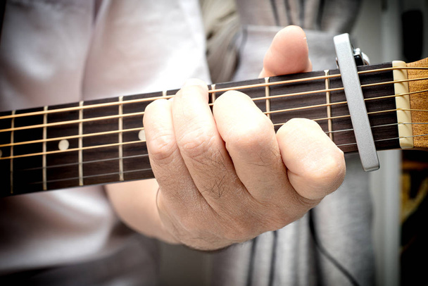 Крупным планом пальцы мужчины помещены на лад акустической гитары
 - Фото, изображение