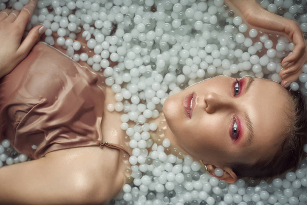Blonde woman posing in water with balls. - 写真・画像