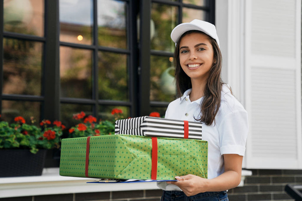 Deliverywoman holding gift boxes and folder. - Φωτογραφία, εικόνα