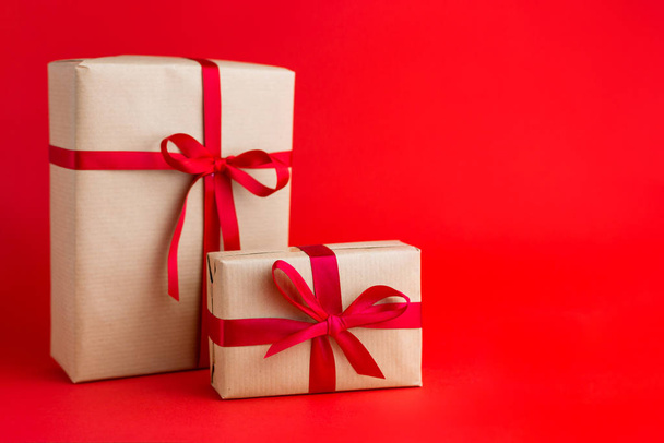 zwei braune Geschenkboxen mit roten Bändern auf rotem Hintergrund. Geschenk zu Weihnachten, Valentinstag oder Geburtstag. - Foto, Bild