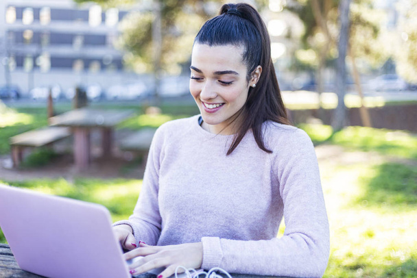 Young beautiful woman sitting outdoors while working with laptop - Фото, изображение