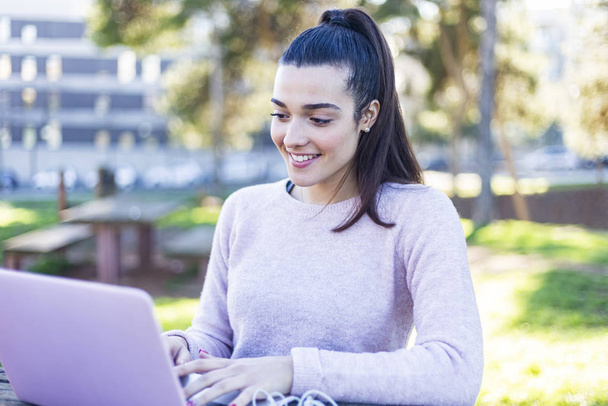 Young beautiful woman sitting outdoors while working with laptop - Foto, imagen