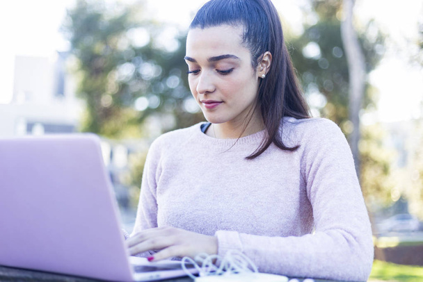 Young beautiful woman sitting outdoors while working with laptop - Zdjęcie, obraz