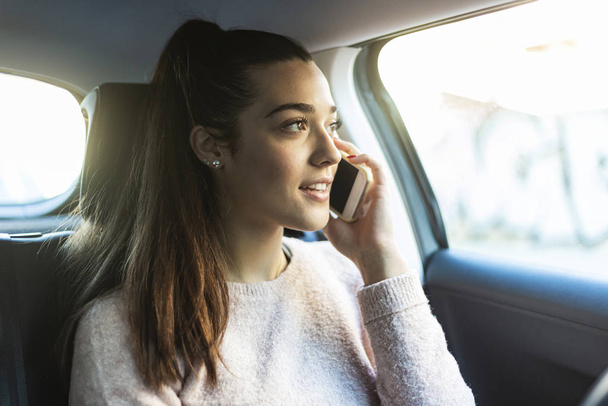 Young beautiful woman with ponytail talking on the phone in the back seat of car - Photo, Image