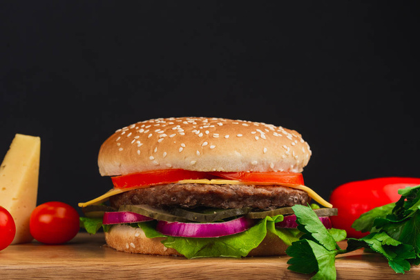 Вид крупным планом, вкусный гамбургер с помидорами, сыром, огурцами и салатом на деревянном столе
 - Фото, изображение