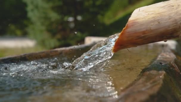 Pomalý pohyb: Křišťálově čistý proud vody teče dřevěnou trubkou do umyvadla - Záběry, video