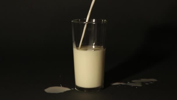 melk in een beker gieten op een geïsoleerde donkere achtergrond - Video