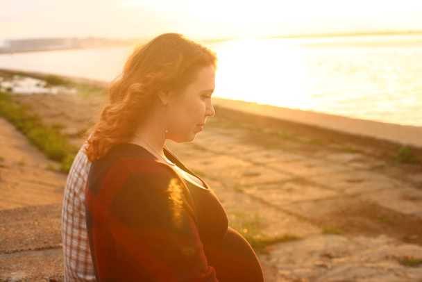 молодая женщина с вьющимися рыжими волосами на девятом месяце беременности
 - Фото, изображение