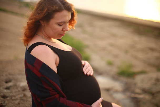 mladá žena s kudrnatými zrzavými vlasy v devátém měsíci těhotenství - Fotografie, Obrázek