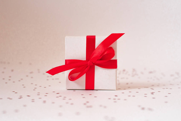 Подарочная белая коробка с красной атласной лентой, луком и звездами на белой нитке
 - Фото, изображение