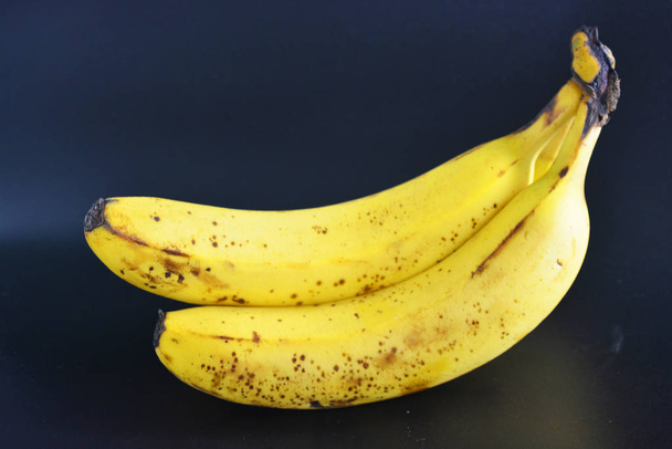 Zoete rijpe gele bananen, een bos van drie bananen met zwarte pegmet vlekken bevinden zich op een zwarte plastic achtergrond. Juiste voeding, gezond smakelijk fruit voor elke dag. - Foto, afbeelding