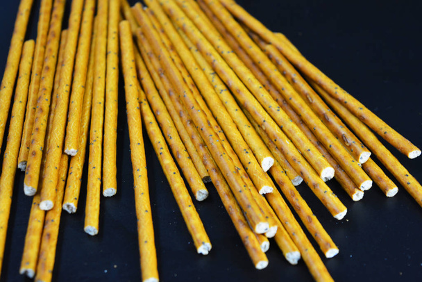 Tasty and sweet straws with poppy seeds made of flour, sneking scattered on a black plastic background. - Foto, imagen