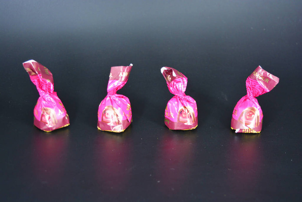 Doces doces e saborosos com conhaque e cereja em embalagens roxas estão localizados em um fundo de plástico preto fosco
. - Foto, Imagem