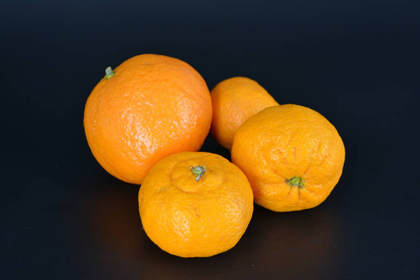 Smaczne i zdrowe owoce, trzy mandarynki i jeden minerał znajdują się na czarnym plastikowym tle. - Zdjęcie, obraz