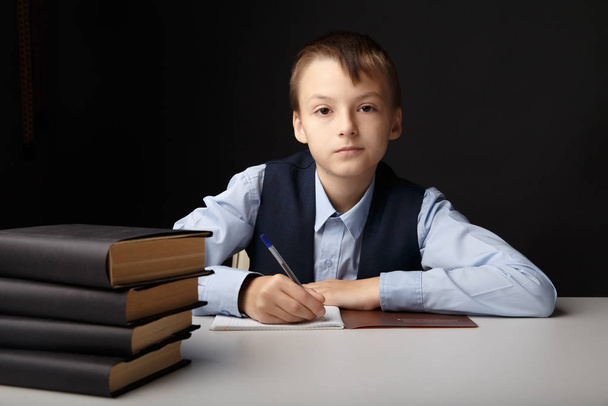 Освіта в шкільній концепції. Хлопчик сидить за столом і навчається ізольовано в сірому класі
. - Фото, зображення