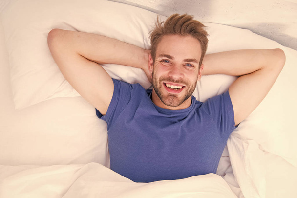 New smile, new day. Happy man awaken in bed. Handsome caucasian man with happy smile relaxing in the morning. Sparkling white smile treatment and aftercare procedure. Smile that fits his lifestyle - Photo, Image