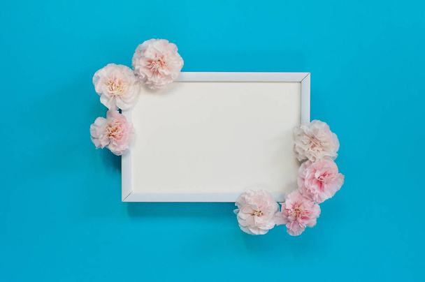 Flat lay - white blank frame with pink carnations on a blue back - Foto, imagen