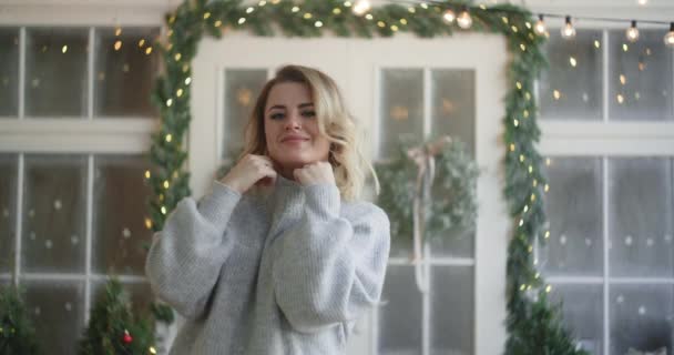 Mujer atractiva europea en ropa de abrigo envuelve en un suéter y mira a la cámara, escandinavo interior de invierno, acogedor ambiente de año nuevo en casa, 4k DCI 120fps Prores HQ
 - Metraje, vídeo