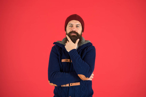 Winter menswear. Man bearded warm jumper and hat red background. Winter season menswear. Personal stylist. Warm and comfortable. Fashion menswear shop. Masculine clothes concept. Think and decide - Fotó, kép