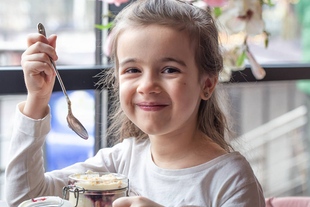 Красивая маленькая девочка ест десерт в кафе
. - Фото, изображение