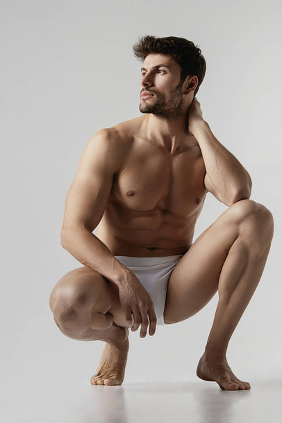 Strong stripped muscle male model in white underwear on gray isolated font background - Φωτογραφία, εικόνα