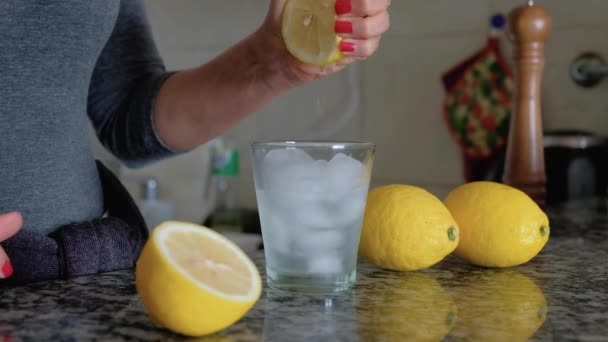 Woman squeezing lemon with both hands on glass with ice between lemons - Footage, Video