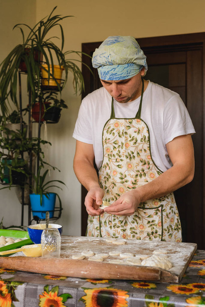Um homem vestido com um avental e chapéu prepara bolinhos na cozinha
. - Foto, Imagem