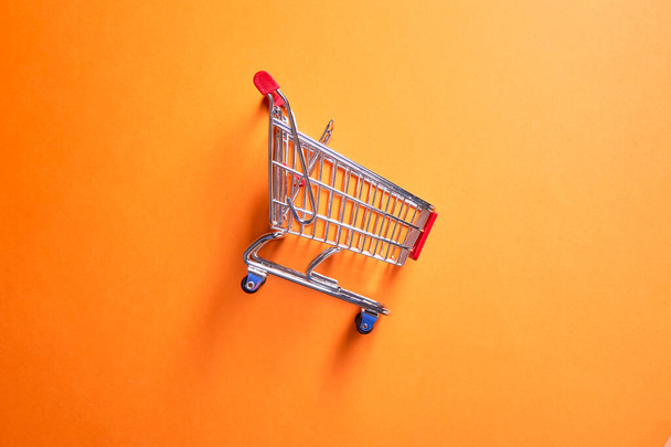 Iron toy supermarket trolley on empty orange background - Valokuva, kuva