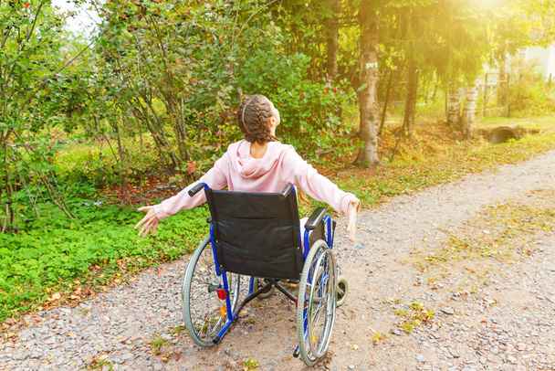 Mladá žena se šťastným handicapem na vozíčku v nemocničním parku si užívá svobody. Paralyzovaná dívka v invalidním křesle pro tělesně postižené v přírodě. Rehabilitační koncept. - Fotografie, Obrázek