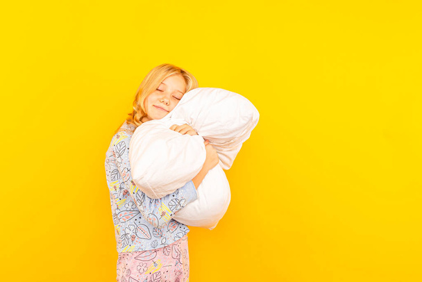 Adorable little girl looking at the camera and hugging a pillow background of a yellow wall - Photo, Image