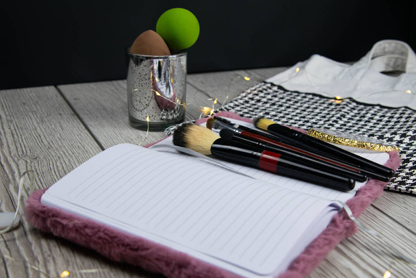 Ouvrir un modèle de carnet de notes vierge, des pinceaux de maquillage et une palette d'ombres à paupières sur une table en bois blanc
 - Photo, image