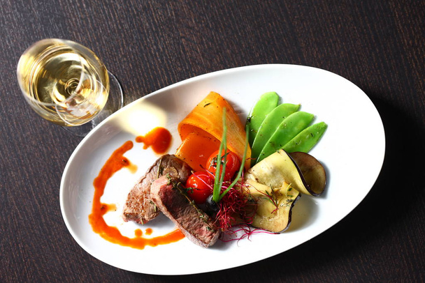 Leckeres Essen auf dem Tisch im Restaurant mit Kopierraum und ovalen Tellern und einem Glas Wein - Foto, Bild