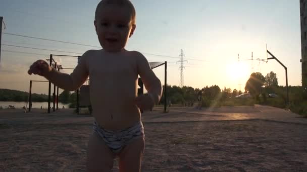 mały zabawny chłopiec w kąpielówkach biegnie i macha rękami przed kamerą - Materiał filmowy, wideo