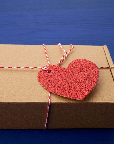 caja marrón rectangular con un regalo y un corazón de papel rojo atado a
  - Foto, imagen
