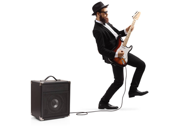 Bearded male artist in a suit playing a plugged electric guitar - Photo, image