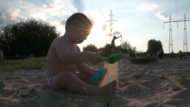 Stad strand in de buurt van elektriciteitsleidingen - Kleine jongen zitten en spelen met een emmer en een schop - Video