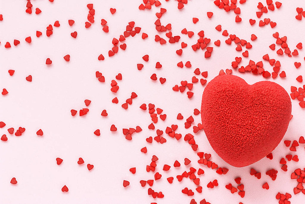 Valentijnsdag concept. Rood hart fluwelen taart op een roze oppervlak met veel mini snoepjes in de vorm van kleine hartjes - Foto, afbeelding