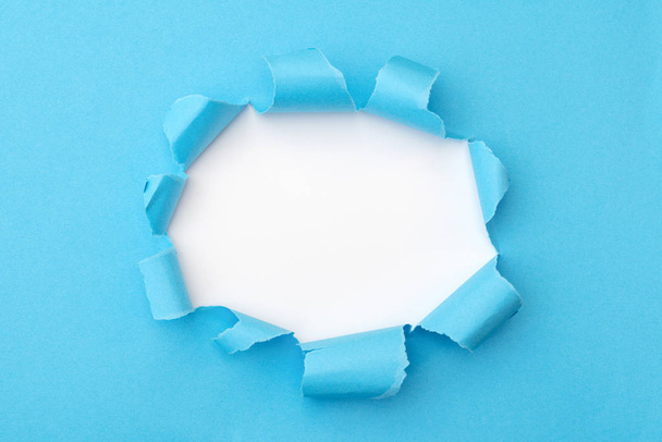Blue paper with ripped hole in the middle background - Photo, Image