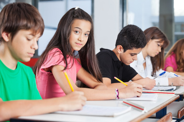 Teenage Girl Sitting With Classmates Writing At Desk - Zdjęcie, obraz